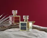 Dwa flakony perfum z etykietami "Dubai Elixir" i "Mamma Mia!", zawierające feromony damskie, stoją na piasku obok kawałka drewna.