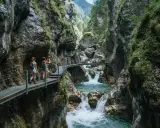 Due escursioniste attraversano passerelle metalliche nel suggestivo orrido di Uriezzo, con un fiume impetuoso che scorre tra le rocce.