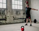 Mężczyzna wykonuje ćwiczenia z kettlebell, idealne dla początkujących. W tle sztanga i surowe wnętrze.