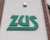 Zielone logo ZUS na białej ścianie budynku z ceglanymi elementami.