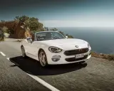 Biały Fiat 124 Spider sunie po krętej drodze nad morzem.