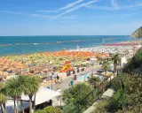 Ampia spiaggia libera a Gabicce Mare, con file infinite di ombrelloni colorati e lettini sotto un cielo azzurro.