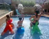 Niños y adultos disfrutan en una piscina con chorros de agua y tobogán. ¡Una idea genial de qué hacer en Salou con niños!