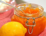 En burk med hemgjord citronmarmelad och en färsk citron på en rödvitrutig duk.