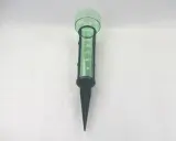 Pluviomètre vert avec graduations pour savoir comment lire un pluviomètre. Il est planté dans le sol.