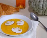 Soupe de courge orange avec des champignons, une serviette orange et une courge entière, évoquant une ambiance de Marina di Chioggia.