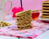 Una pila de tortitas de avena, con un tenedor atravesado, sobre una servilleta floral rosa. Al fondo, una taza y miel.