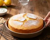 Un délicieux gâteau sans beurre, saupoudré de sucre glace, sort du four. Des citrons et de la crème sont à proximité.