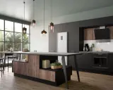 Cuisine fermée avec coin repas moderne, îlot central en bois et noir, réfrigérateur blanc, et grandes fenêtres donnant sur la verdure.