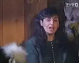 Kobieta z ciemnymi włosami, w zielonej bluzce, mówi do kamery. Chciałabym być tam gdzie ty, w tym przytulnym wnętrzu.
