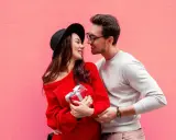 Para zakochanych na tle różowej ściany. Ona trzyma prezent, on obejmuje ją ramieniem. Mówi mu "I love you" po angielsku.