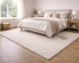 En ljus sovrumsmatta placerad framför en säng med vita sängkläder och en beige pläd.