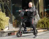 Un homme en tenue de moto est prêt pour un trajet de 10 km en trottinette électrique. Le temps est parfait pour explorer la ville.