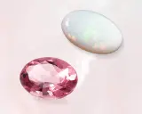 Due gemme ovali, una rosa e un opale, brillano su sfondo chiaro. La pietra rosa ricorda la pietra d'ottobre.