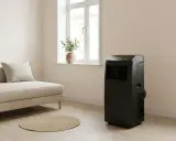 Un salon moderne avec un canapé beige, un tapis rond en jonc et un climatiseur Klarstein noir discret.