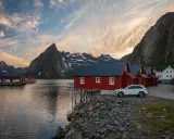 Röda fiskestugor vid vattnet i Lofoten, perfekt boende för en stuga-semester med dramatiska berg i bakgrunden.