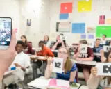 Classe che usa un'app per la scuola, con studenti che mostrano carte con simboli.