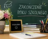 Kwiaty, tabliczka z napisem "DZIĘKUJEMY!" i uśmiechem, stos książek i przybory piśmiennicze na biurku. Na tablicy napis "ZAKOŃCZENIE ROKU SZKOLNEGO".