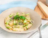 Creamy pasta with asparagus, basil, and grated parmesan cheese in a bowl, with a wedge of parmesan on a cutting board.