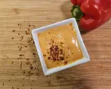Cremige Chipotle-Sauce in einer weißen Schale, bestreut mit Chiliflocken. Daneben liegt eine rote Paprika auf einem Holzbrett.