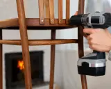 Persona repara una silla de madera con taladro. Un tornillo pasado de rosca dificulta la tarea.