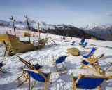 Alpe di Mera: un galeone di legno e sdraio blu attendono i visitatori sulla neve, con montagne innevate sullo sfondo.
