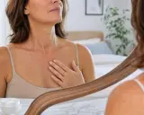 Une femme examine son décolleté dans un miroir, sa main effleurant doucement les rides.