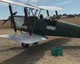 Grüner Doppeldecker, bereit zum Start. Ein Pilot und ein Passagier sitzen im Cockpit. Das Flugzeug erinnert an einen Tiger Moth.