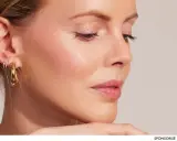Profil d'une femme avec une peau éclatante, des boucles d'oreilles dorées et un maquillage subtil.