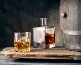 Szklanka z lodem i butelka whisky obok drewnianej beczki. Idealne połączenie, by dowiedzieć się, z czym pić whisky.
