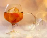 Ein Glas mit bernsteinfarbenem Brandy und Eiswürfeln steht neben einem leeren, umgekippten Glas. Was ist ein Brandy? Ein edles Getränk.