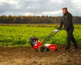 Mężczyzna pracuje glebogryzarką, spulchniając ziemię na polu. Glebogryzarka do czego służy? Do przygotowania gleby pod uprawę.