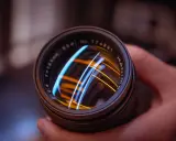 Primer plano de un objetivo fotográfico con reflejos de luces azules y naranjas.