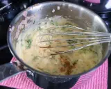 En kastrull med en krämig bearnaisesås som vispas med en ballongvisp. Små bitar av schalottenlök och färska örter syns i såsen.