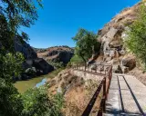 Sendero con barandilla de metal junto a un río y rocas, ideal para rutas senderismo Toledo.