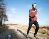 Mann joggt bei 10 Grad in einer leichten Jacke und Hose auf einem Feldweg.