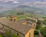 Borghi collinari perfetti per gite in giornata da Reggio Emilia. Un campanile svetta tra tetti antichi e dolci pendii verdi.