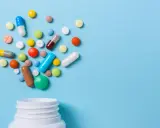 Różnorodne tabletki i kapsułki wysypujące się z białego pojemnika. Czy to opioidy, co to za leki?