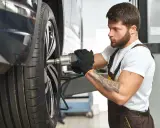 Mechanik z tatuażem dokręca śrubę koła. Zwróć uwagę na objawy zużycia sworznia wahacza, gdy słyszysz stuki.