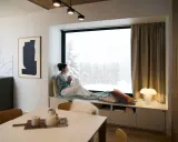 Femme savourant une boisson chaude dans un coin lecture cocooning, regardant la neige tomber.