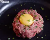 Delicioso steak tartar de wagyu con yema de huevo y cebollino picado, servido en un plato negro.