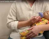 Nauka, jak karmić noworodka butelką, jest kluczowa. Na zdjęciu widzimy, jak prawidłowo karmić niemowlę butelką, trzymając je w ramionach.
