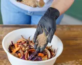 Ajout de bran de riz pour le bokashi maison. Des restes de légumes colorés attendent dans un bol blanc.