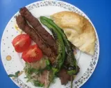 Adana Kebap mit gegrillten Peperoni, Tomaten und Fladenbrot auf einem Teller.