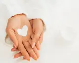 Dłonie w białym szlafroku, z kremem w kształcie serca. Koniec z pękającą skórą na palcach dzięki tej pielęgnacji.