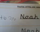 Siedmiolatek ćwiczy pisanie imienia "Noah" w lustrzanym odbiciu. Obok widać próbę pisania imienia.