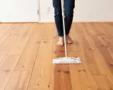 Persona descalza limpiando parquet con una mopa. El suelo de madera luce brillante y cuidado.