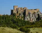 Das Castillo de Loarre thront majestätisch auf einem Felsen, umgeben von grünen Wäldern und unter blauem Himmel.