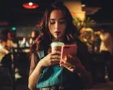 Dziewczyna popija kawę, przeglądając telefon. Może właśnie czyta, że jej facet przestał się odzywać z dnia na dzień.