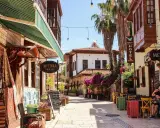 Bunte Gassen in der antalya altstadt mit Teppichläden, Palmen und einem Café, wo ein Mann entspannt sitzt.